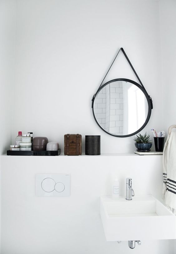Espejo redondo de metal negro en baño blanco de estilo nórdico